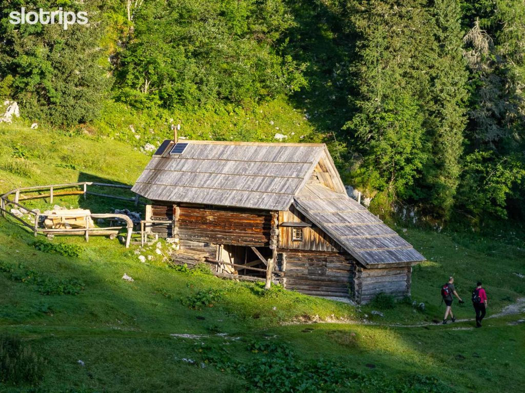 A couple hiking past a shepherd's cabin at Vogar mountain pasture above Lake Bohinj in the Julian Alps in Slovenia