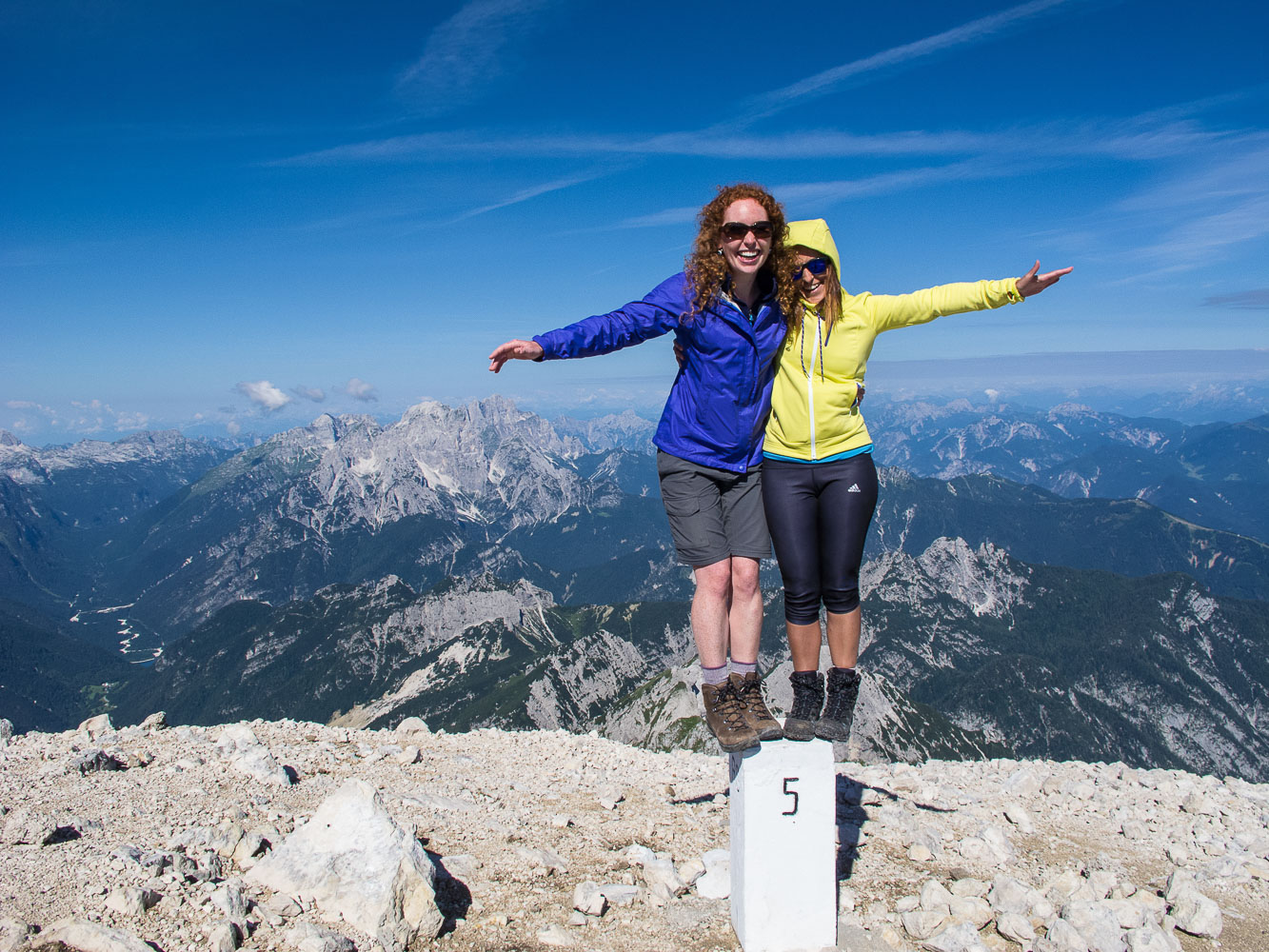 A couple of travelers on a border stone between Slovenia and Italy at the top of Mt. Mangart in the Julian Alps, high above the Soca Valley