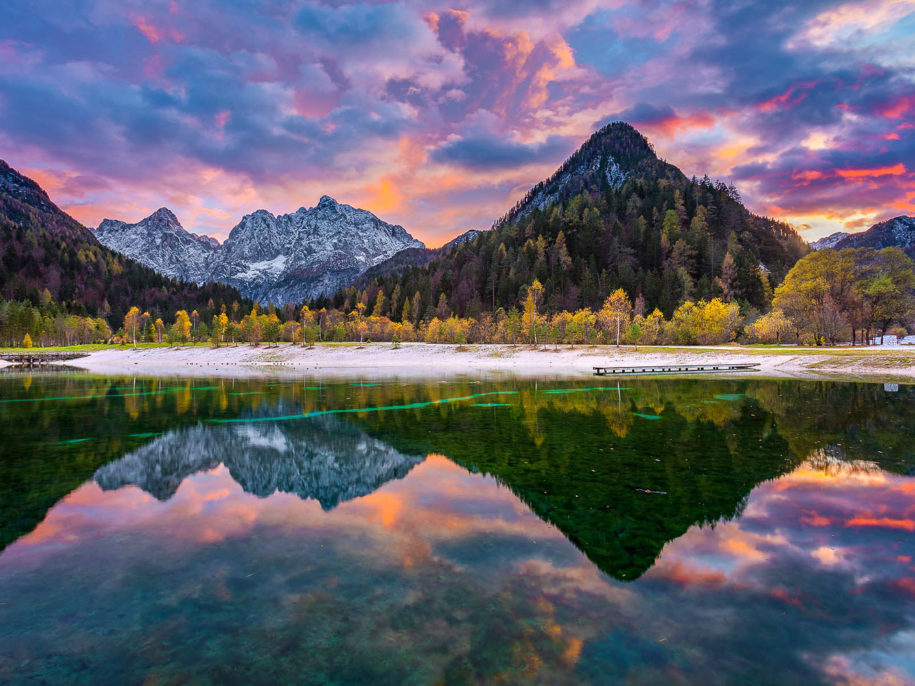 Fantastic colorful caption of autumn nature with mountains and sunset skies mirroring in the Lake Jasna on a photography day trip near Kranjska Gora.