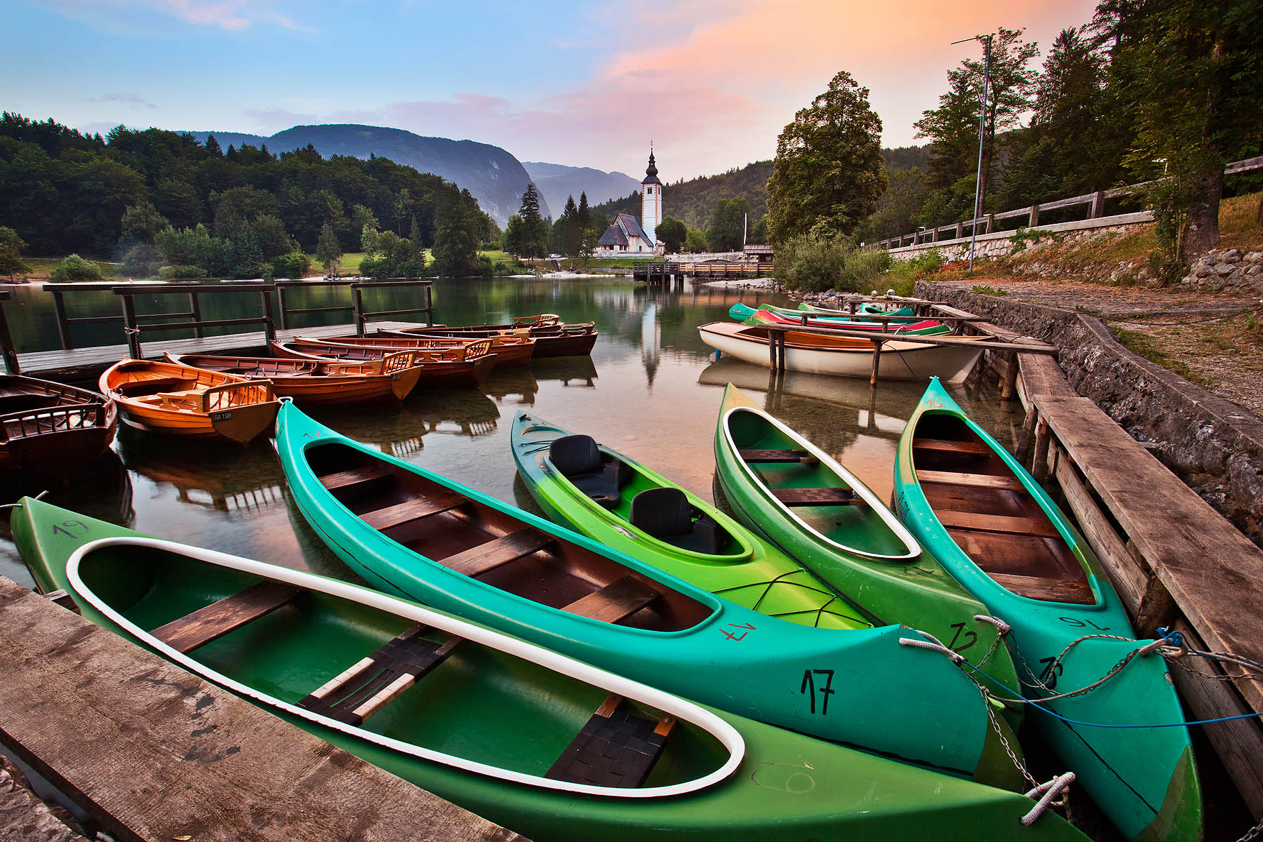 A group of anchored canoes at Lake Bohinj with the Church of St. John the Baptist in the background