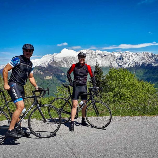 Two road cyclists on an amazing trip across the western Slovenia on a smooth asphalt road at high altitude with snow-capped mountains of the Julian Alps in the background