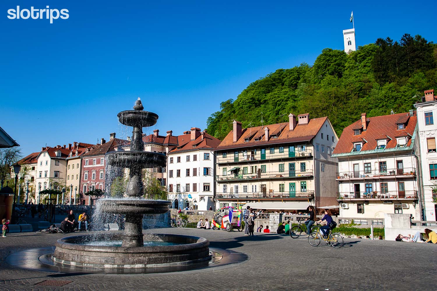 A water fountain on the Novi trg square in Ljubljana city centre with Ljubljanica river canal in the background
