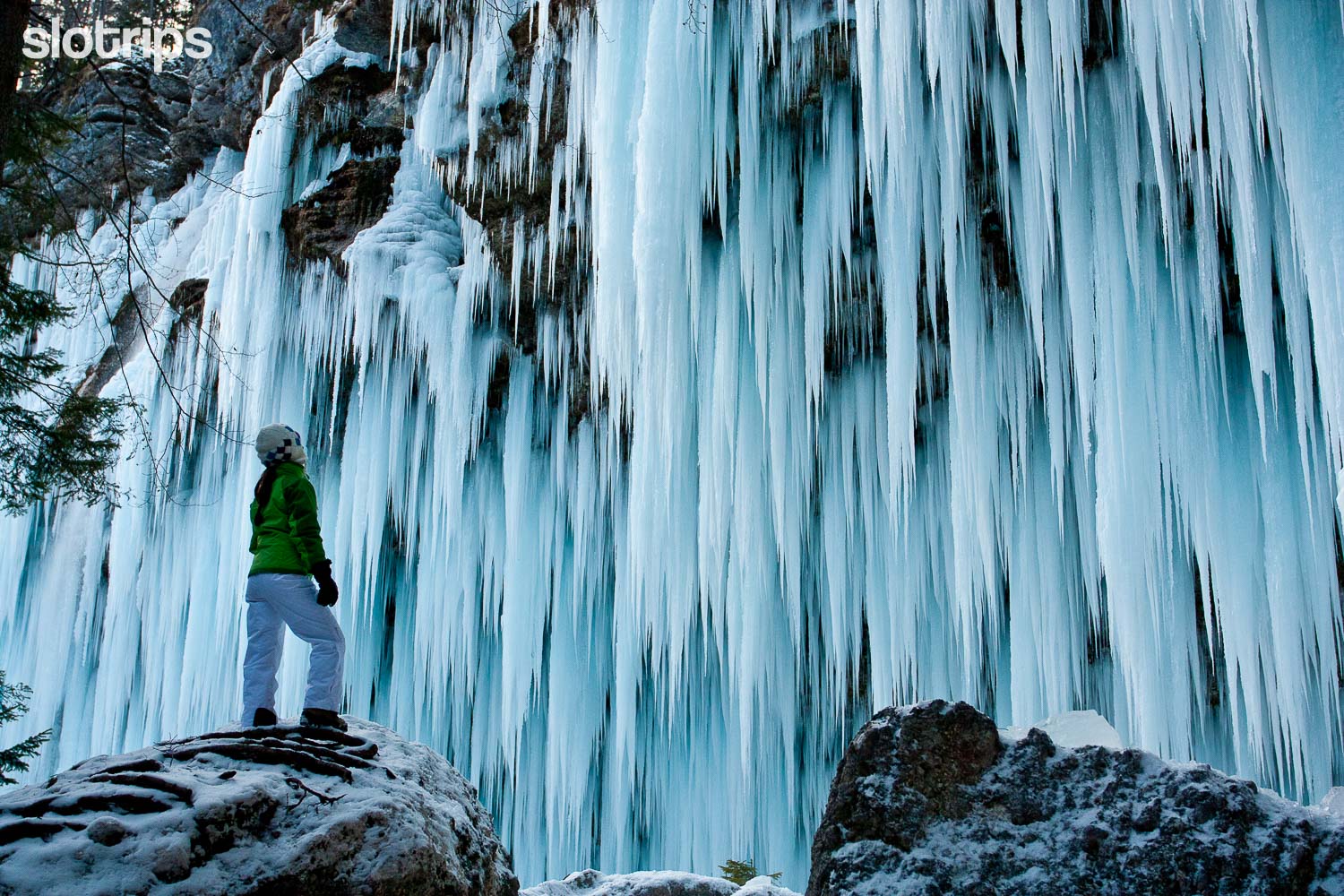 A hiker in front of an ice wall of icicles formed from the Pericnik Waterfall in the Vrata Valley in Triglav National Park, Slovenia