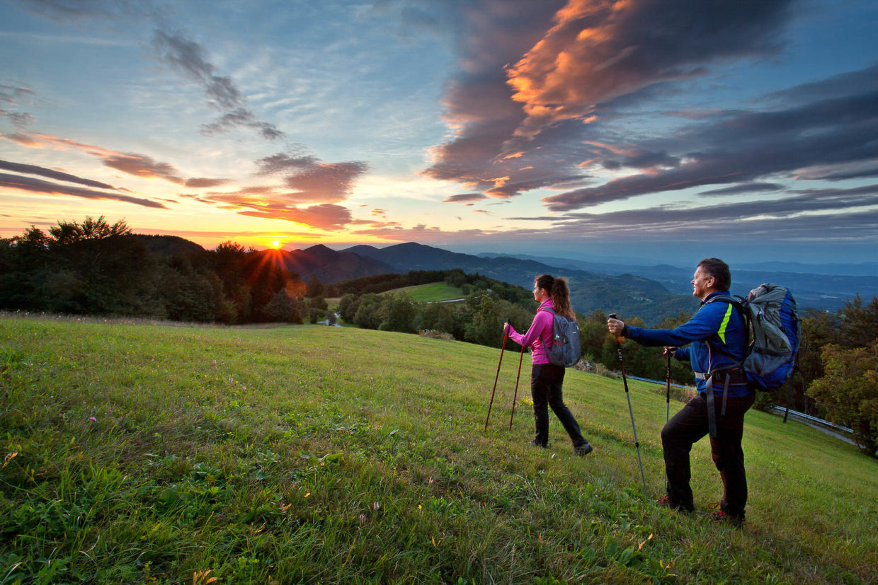 Hikers walking across the green meadows of Lisca hiking trail in Posavje region with a beautiful sunset.