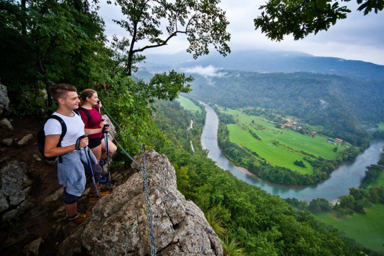 Hikers enjoying the misty view of the Kolpa river meanders from the rock cliff in Bela Krajina.