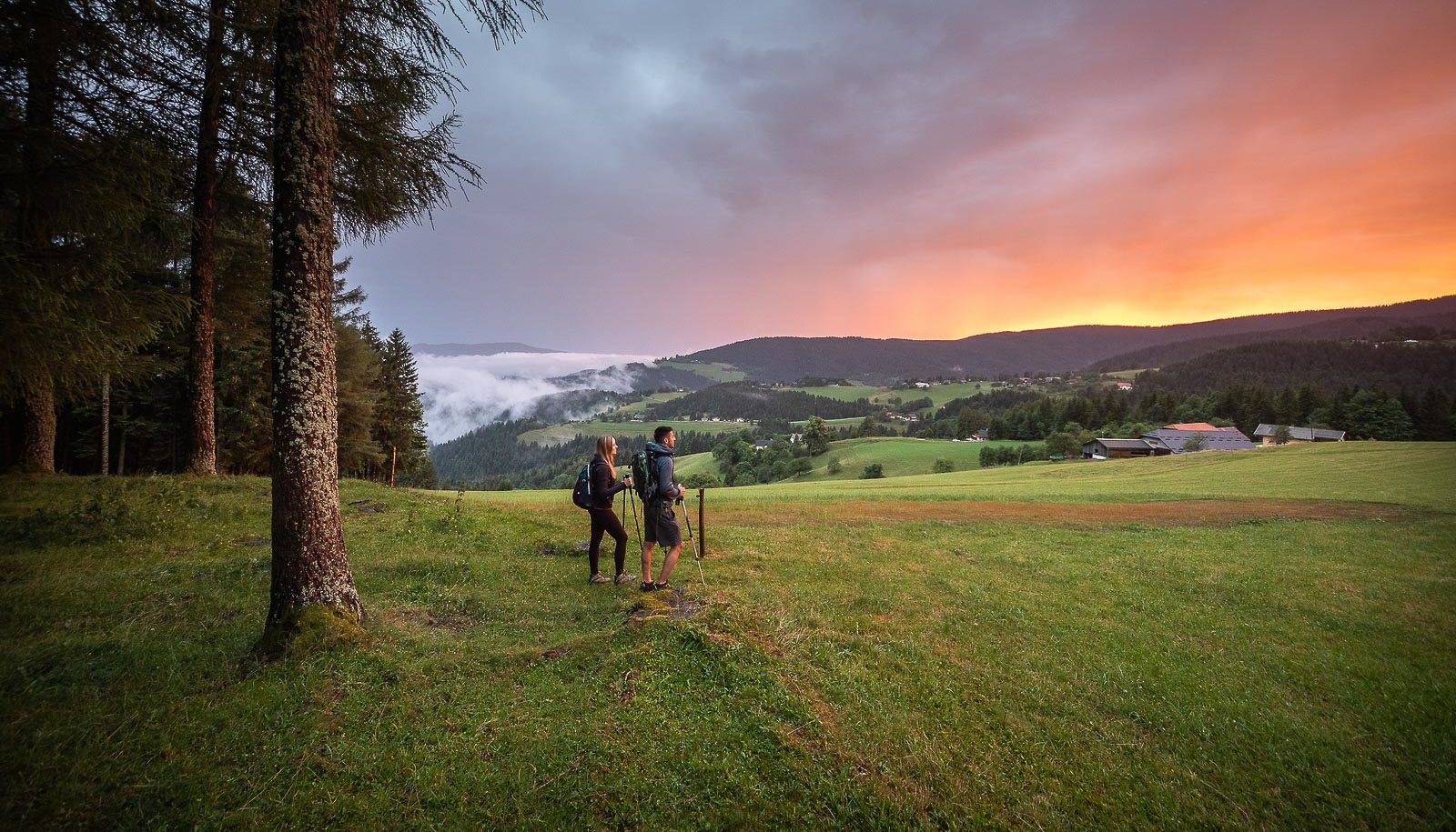 A couple on a walking trip across Pohorje hills enjoying colorful sunset in the countryside of Rogla.