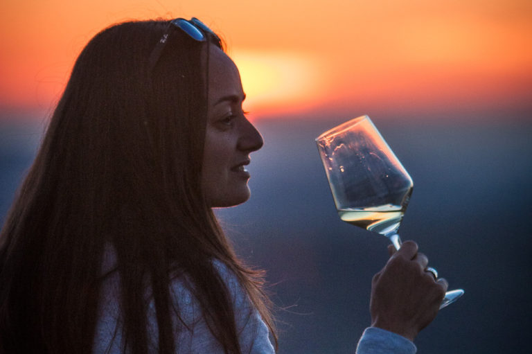 Female traveller enjoying a glass of wine in the colorful orange and violet sunset.