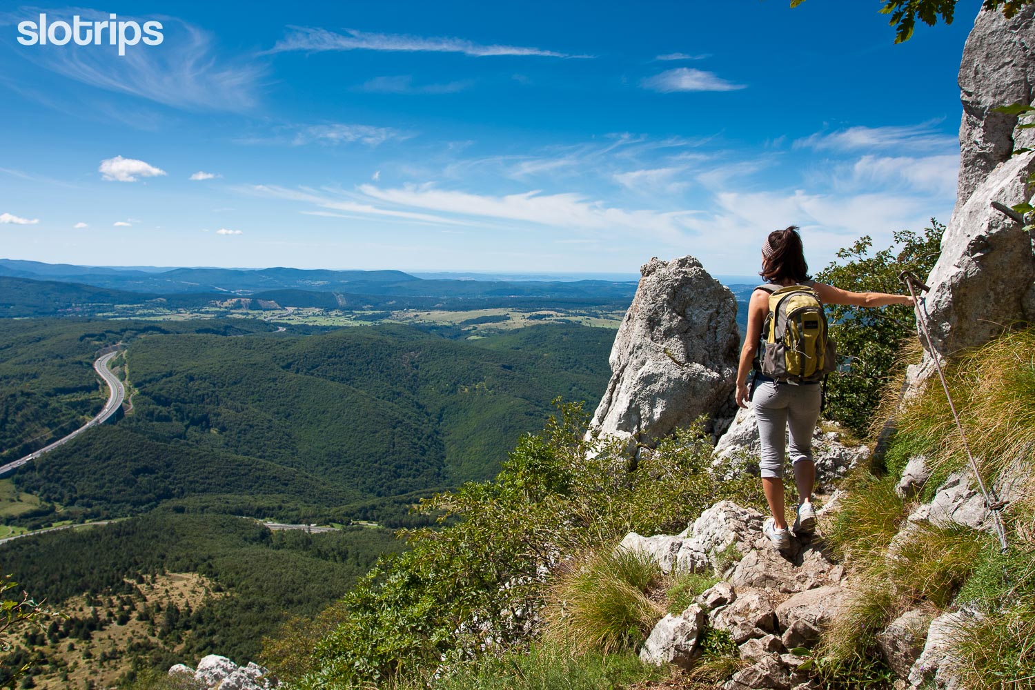Hiker on a cliff of the Mount Nanos via ferrata trail enjoys the beautiful panorama view over the wooded hills of Primorska region on a sunshiny day.