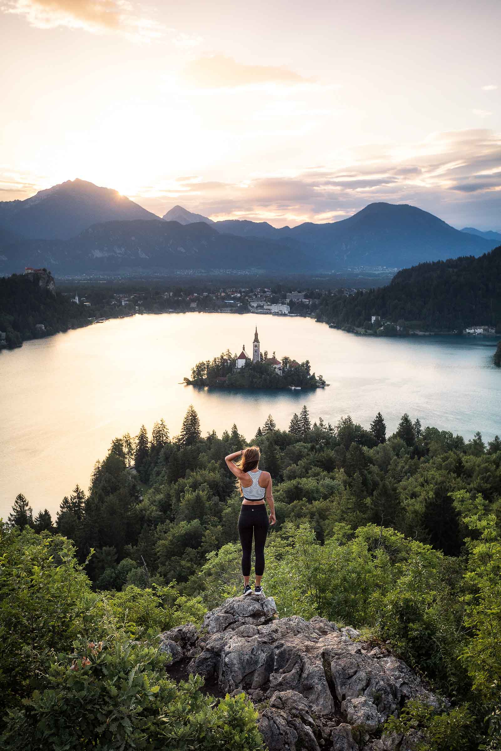 A girl overlooking Lake Bled with Bled castle and Karawanks in the background from Ojstrica viewpoint on a sunrise, Slovenia