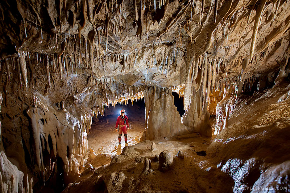 Caver standing in the cave opening, admiring karstic phenomenon of the cave hall with beautiful stalactites and stalagmites.