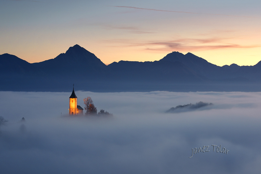Illuminated Jamnik church rising above the morning fog, backed with the Kamnik-Savinja Alps.