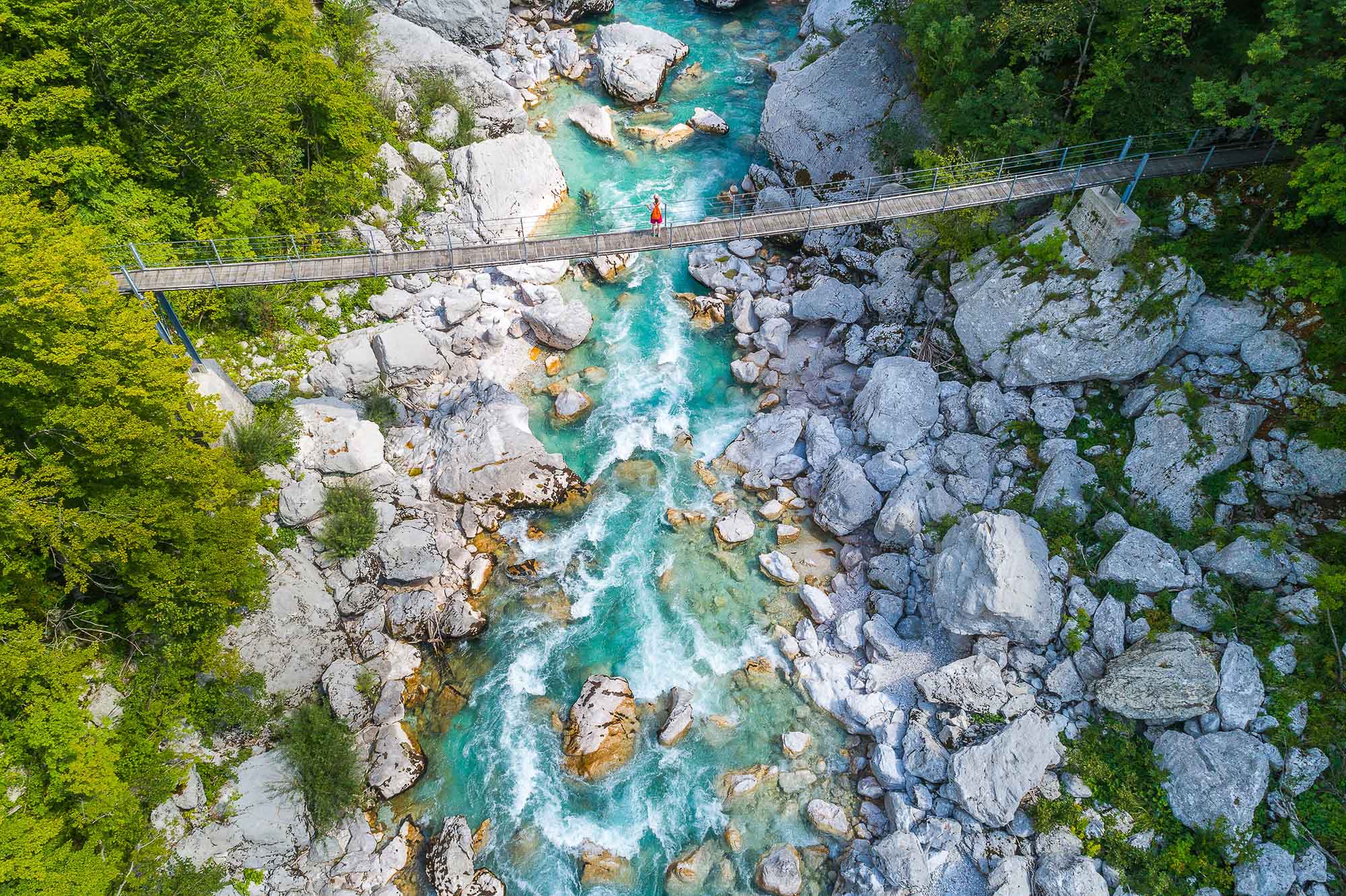 An aerial shot of a girl crossing a bridge over the Soca River on the way to Kozjak waterfall in Soca valley in Slovenia