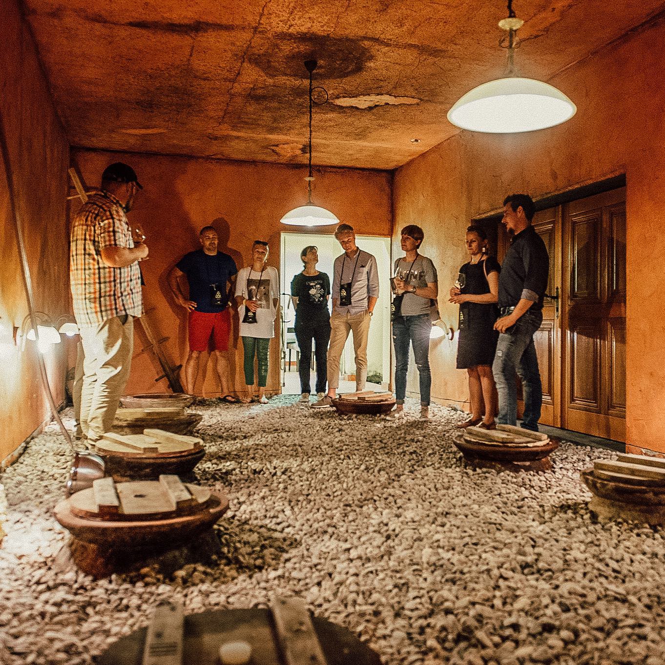 A group at a wine tasting in a dimly lit wine cellar with clay amphoras buried in a local soil in Goriska Brda wine region in Slovenia
