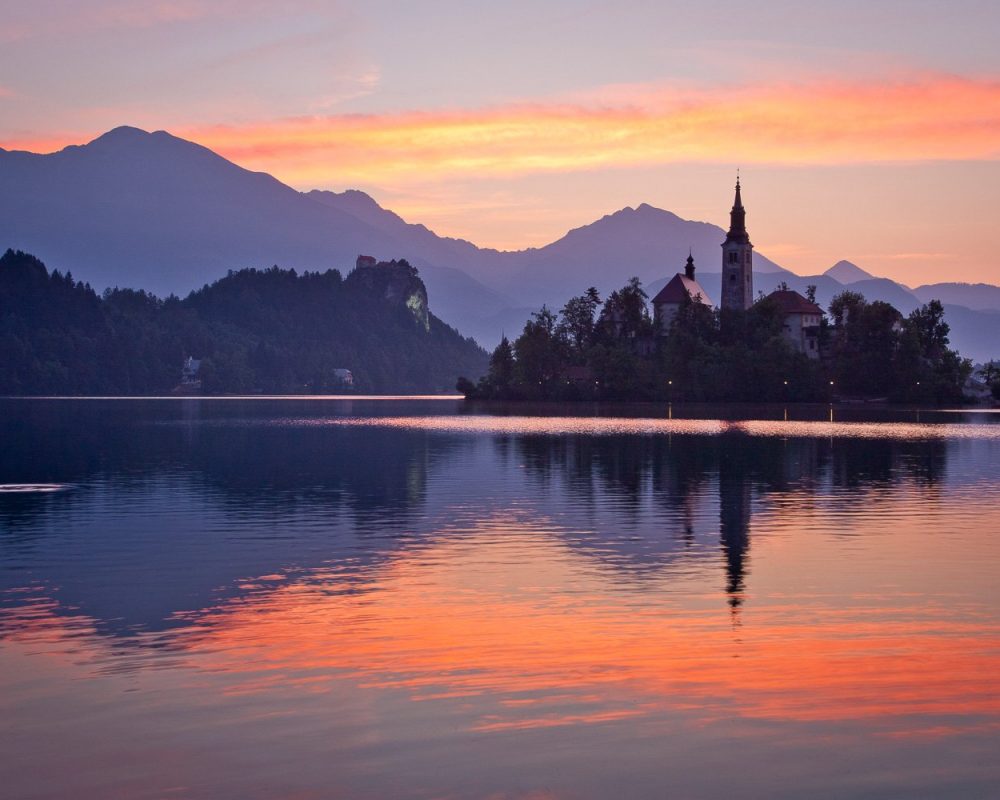 Lake Bled with the Church of the Mother of God on the Lake in the foreground and Bled castle in the background at dawn