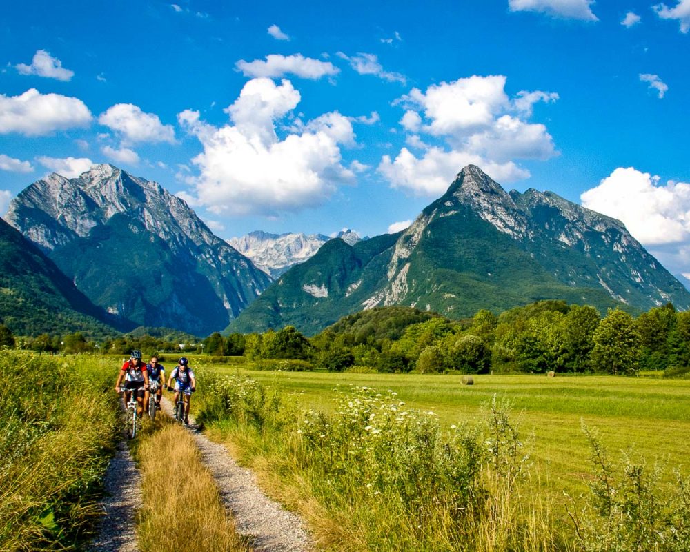 A group of mountain bikers on a gravel road close to the alpine town of Bovec with Mt. Rombon and Mt. Svinjak in the background in the Julian Alps in Slovenia