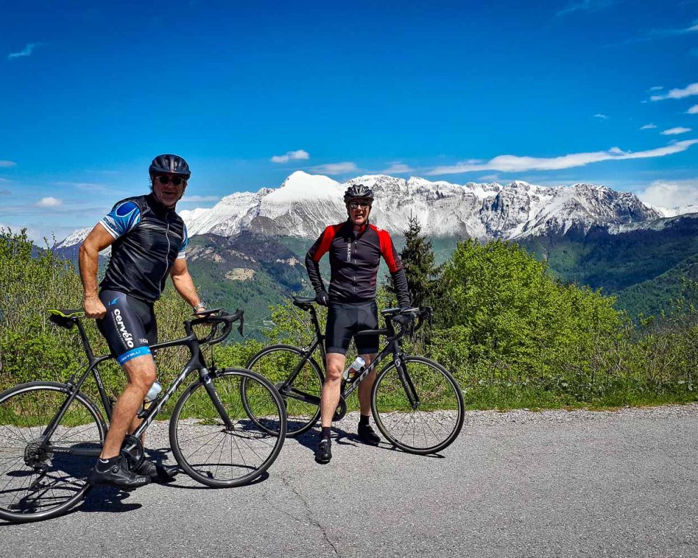 Two road cyclists on an amazing trip across the western Slovenia on a smooth asphalt road at high altitude with snow-capped mountains of the Julian Alps in the background