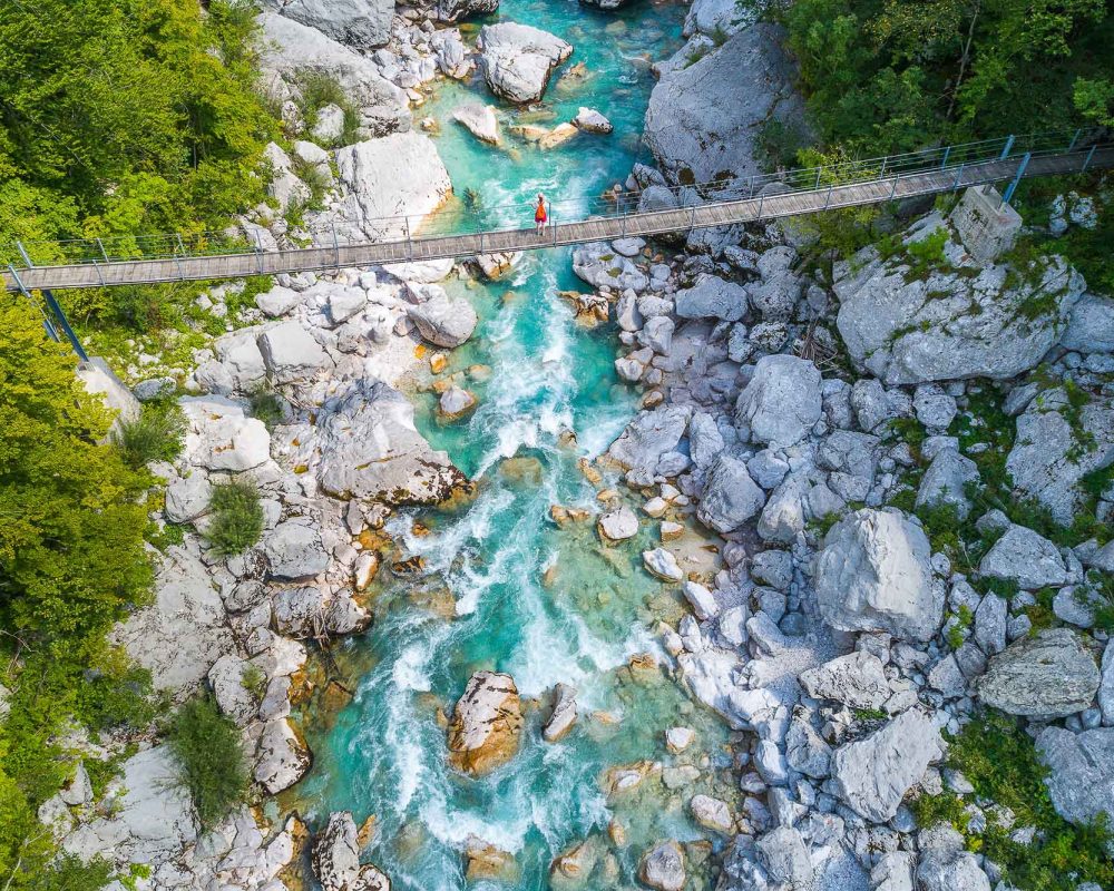 An aerial shot of a girl crossing a bridge over the Soca River on the way to Kozjak waterfall in Soca valley in Slovenia
